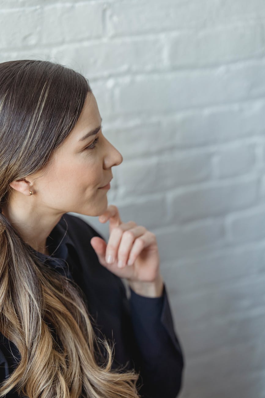 thoughtful woman with long wavy hair near white wall