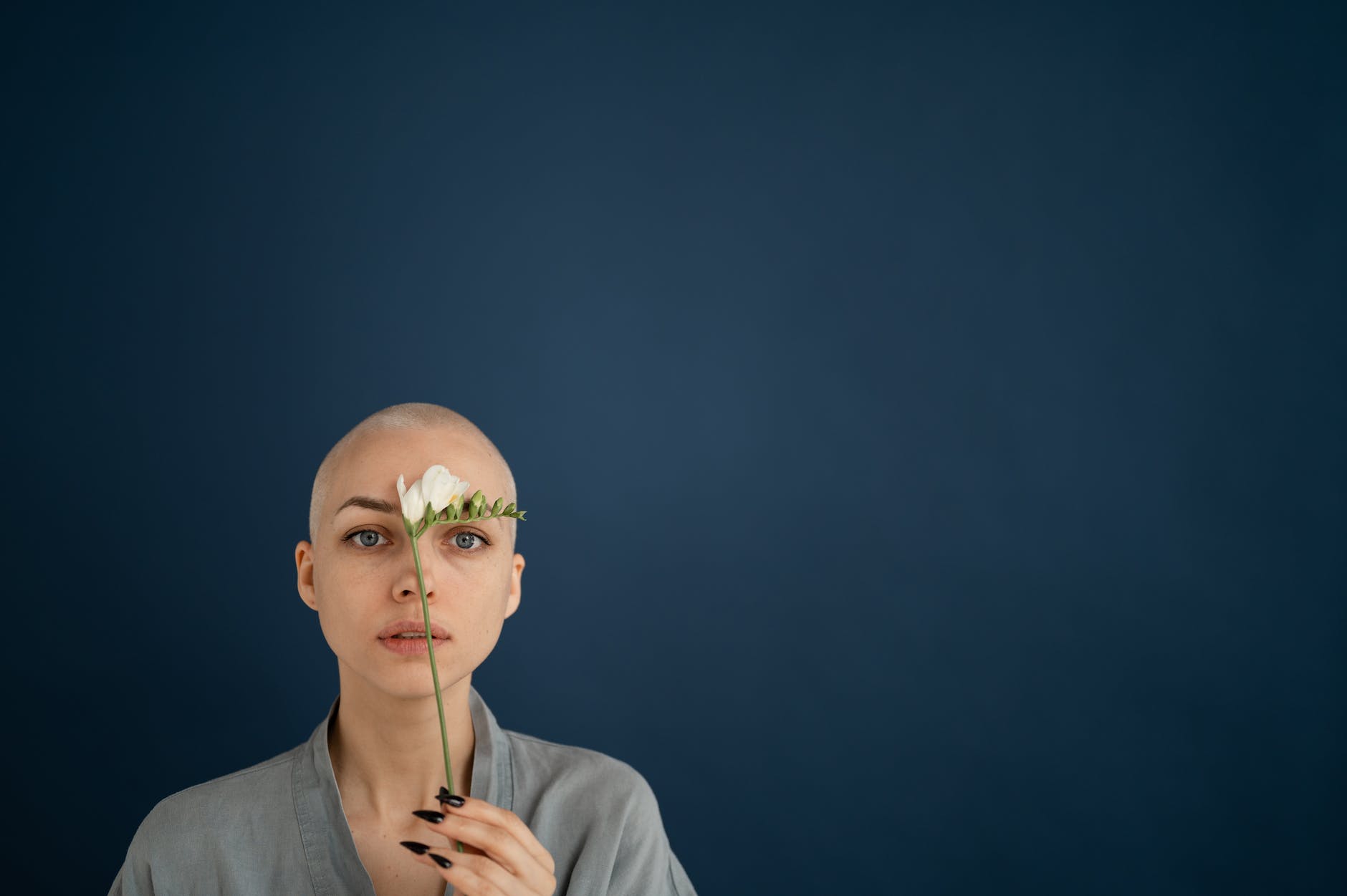 woman with blossoming freesia and shaved head on blue background